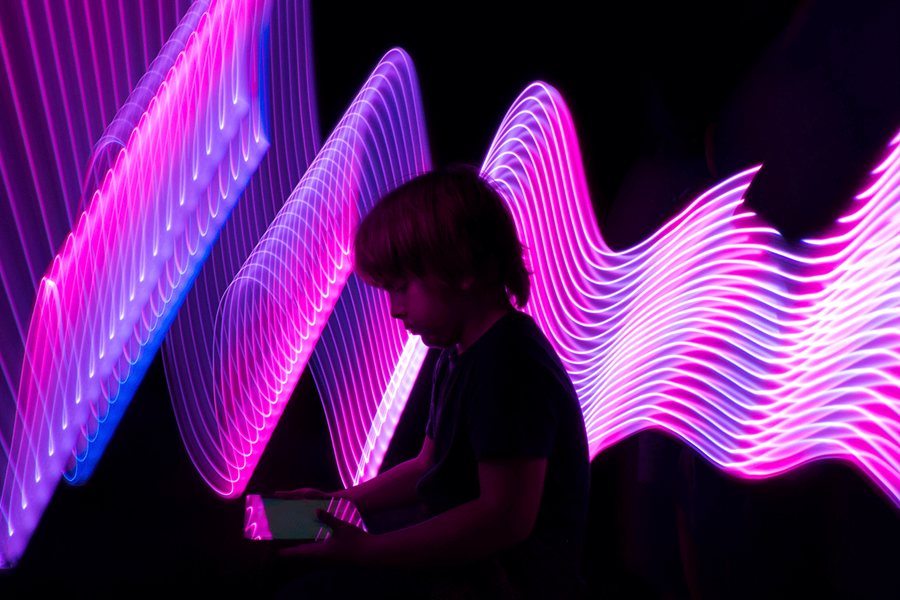 Boy with tablet in front of neon light wall