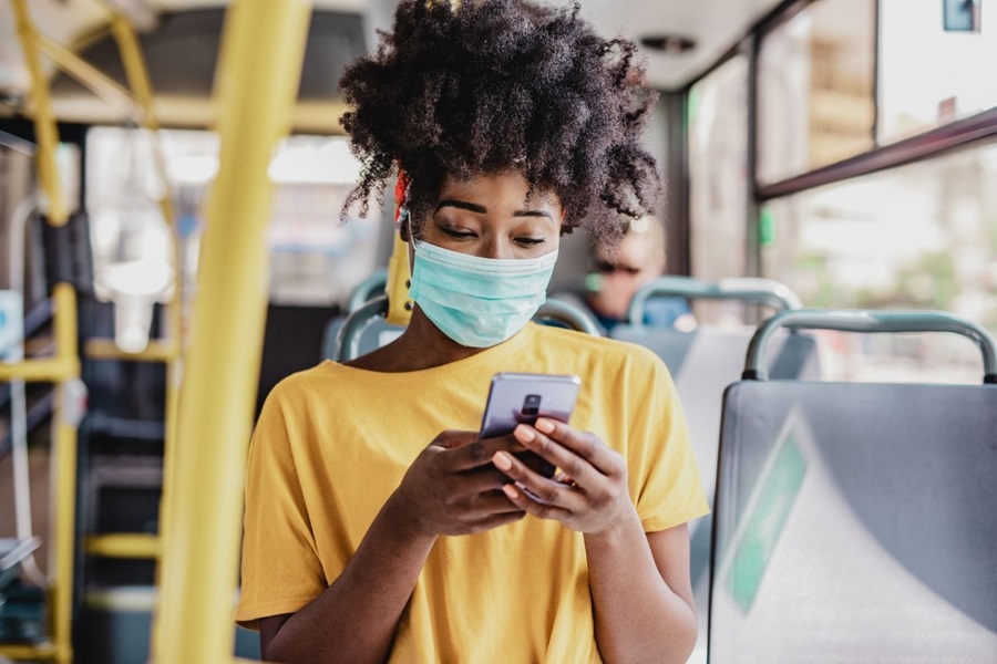 Woman in mask and yellow t-shirt looking at her phone on London bus summertime