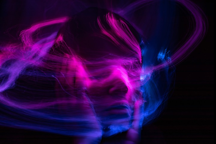 blue, pink, and purple strokes of colour against a black background resembling a person caressing their face.