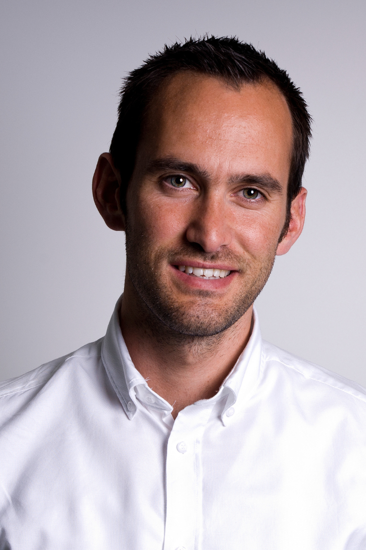 A man with short dark spiky hair, wearing a white shirt, smiling at the camera.