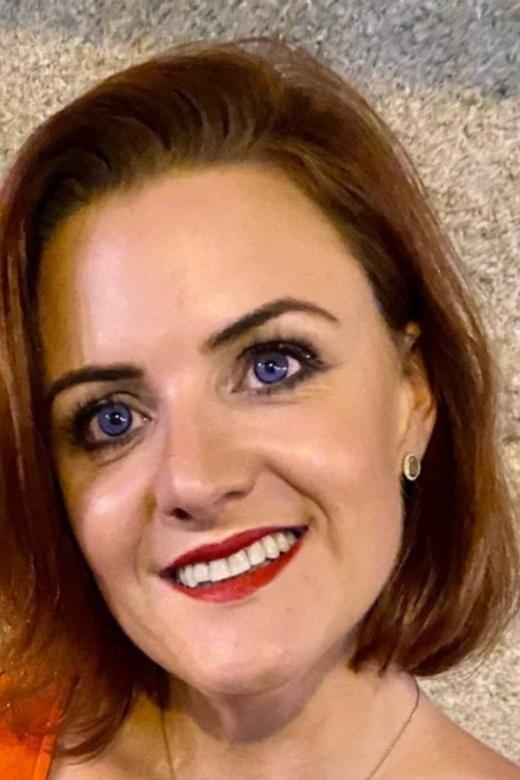 A headshot of Christine, smiling at the camera. She has short auburn hair and blue eyes. 