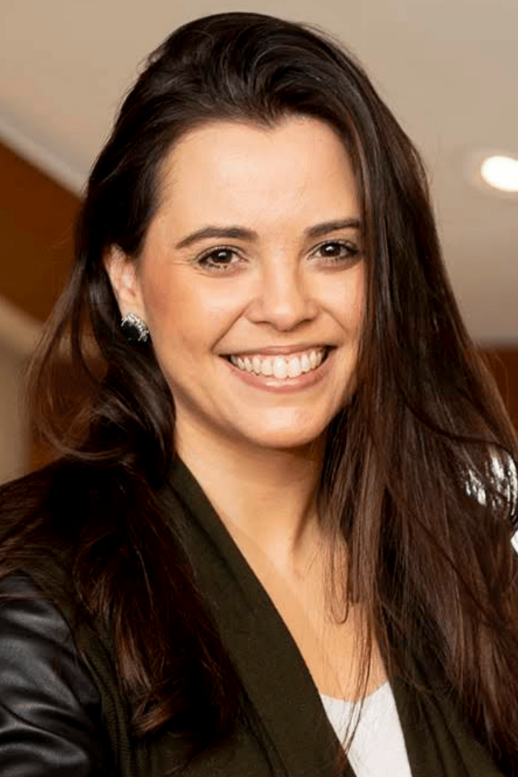 A woman smiling at the camera with long brown hair, wearing a black jacket