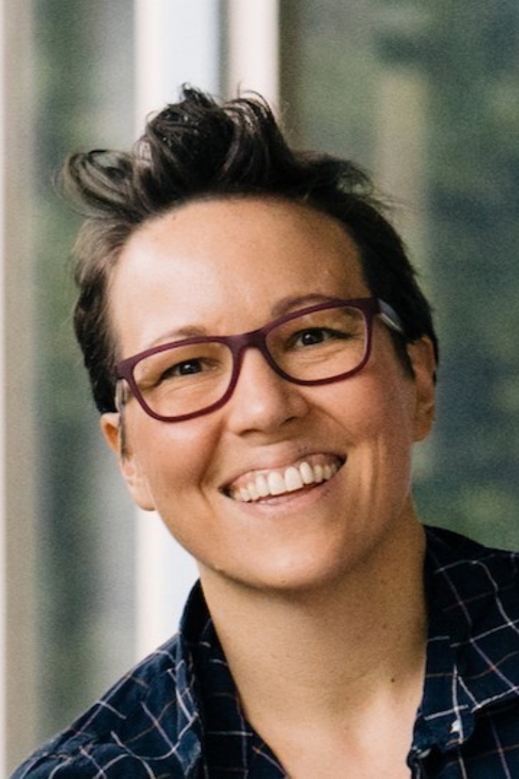 A headshot of Valerie smiling at the camera. She is wearing a blue check shirt, and has glasses. 