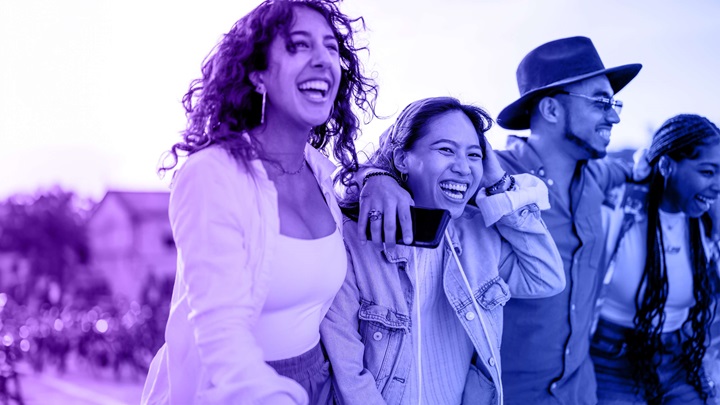 The image depicts four individuals standing closely together with their arms around each other, conveying a strong sense of camaraderie and connection.