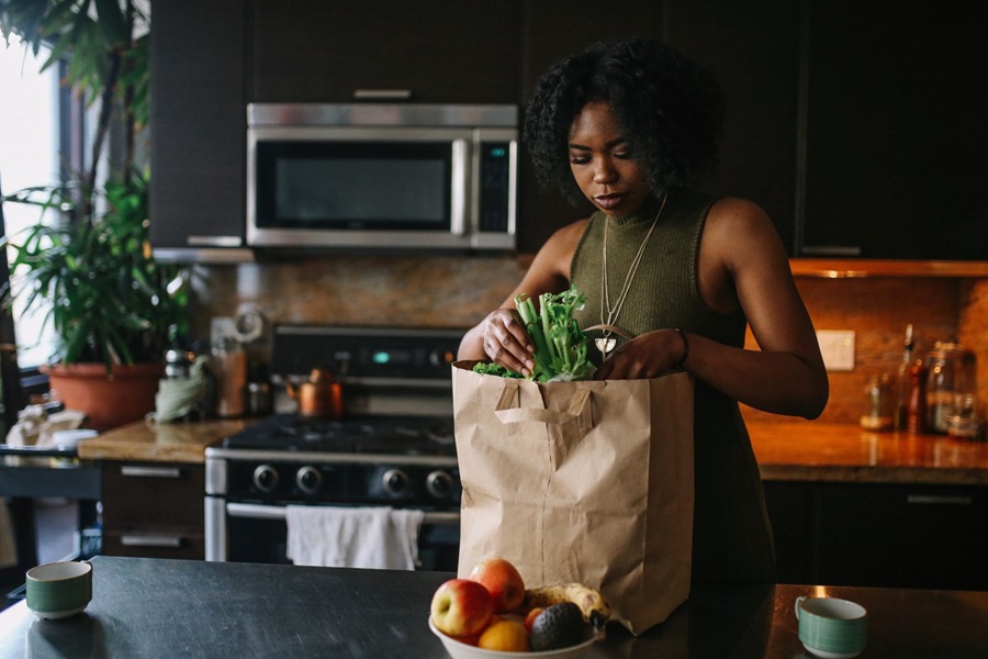 Woman unpacking fruit from a brown paper shopping bag in kitchen 