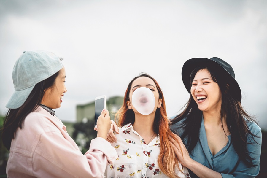 Happy Asian friends having fun chewing bubble gum outdoor