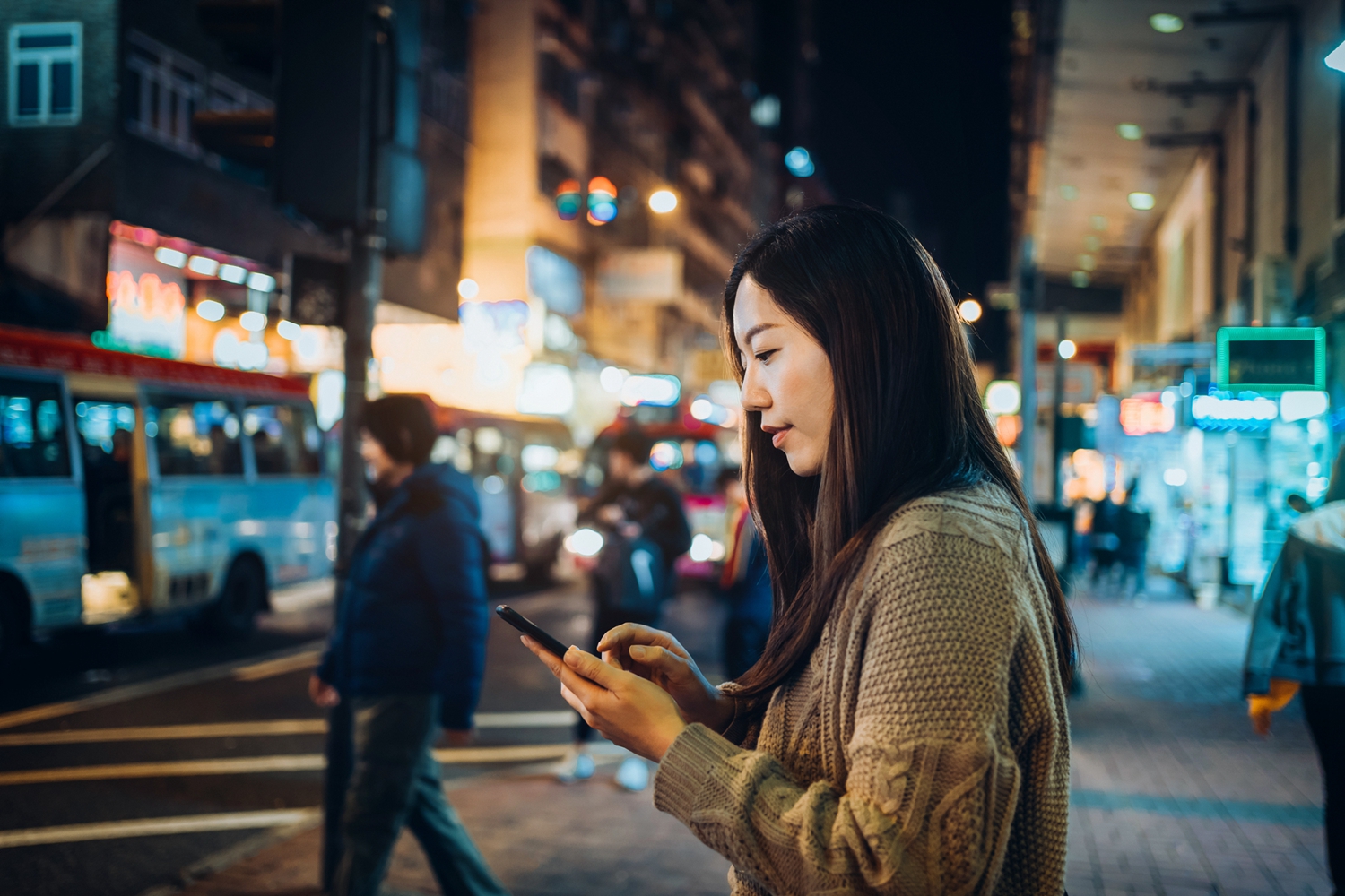 Young Asian woman using smartphone while commuting in city street