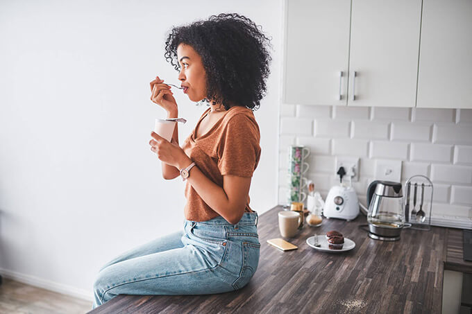 Woman eating yoghurt on a kitchen countertop