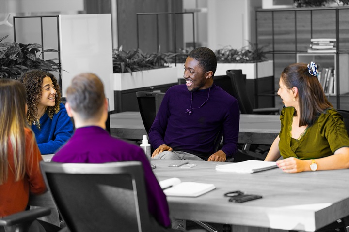 A group of five young employees having a discussion at a table. Three woman and two men.