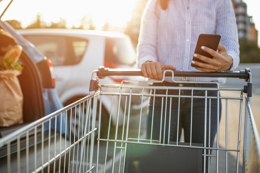 A woman in a white shirt holding a phone while pushing a shopping trolley