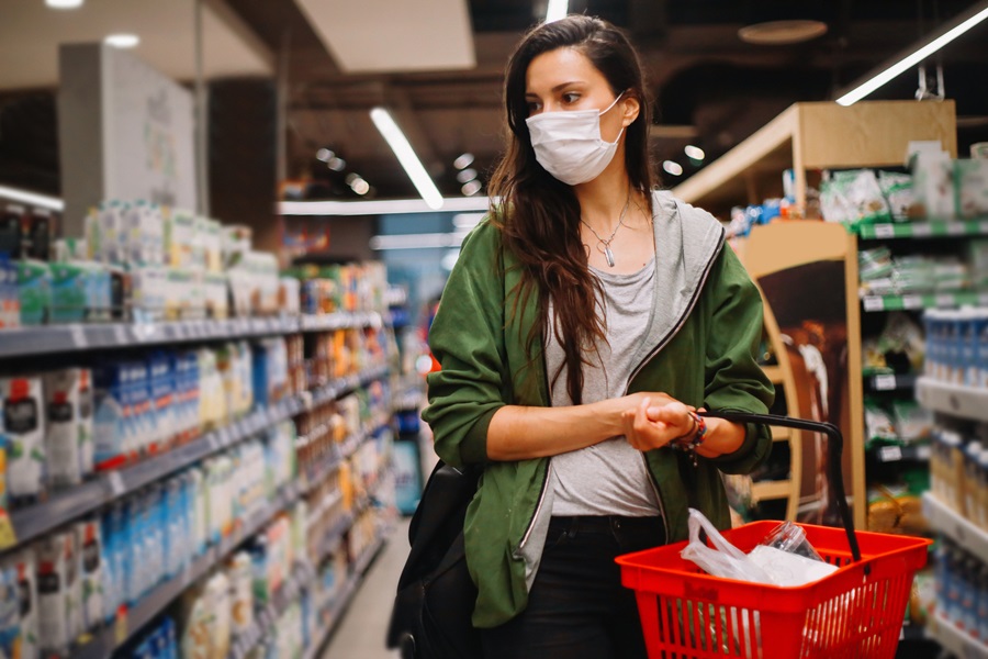 Young woman with red shopping basket in supermarket, she is wearing a facemask